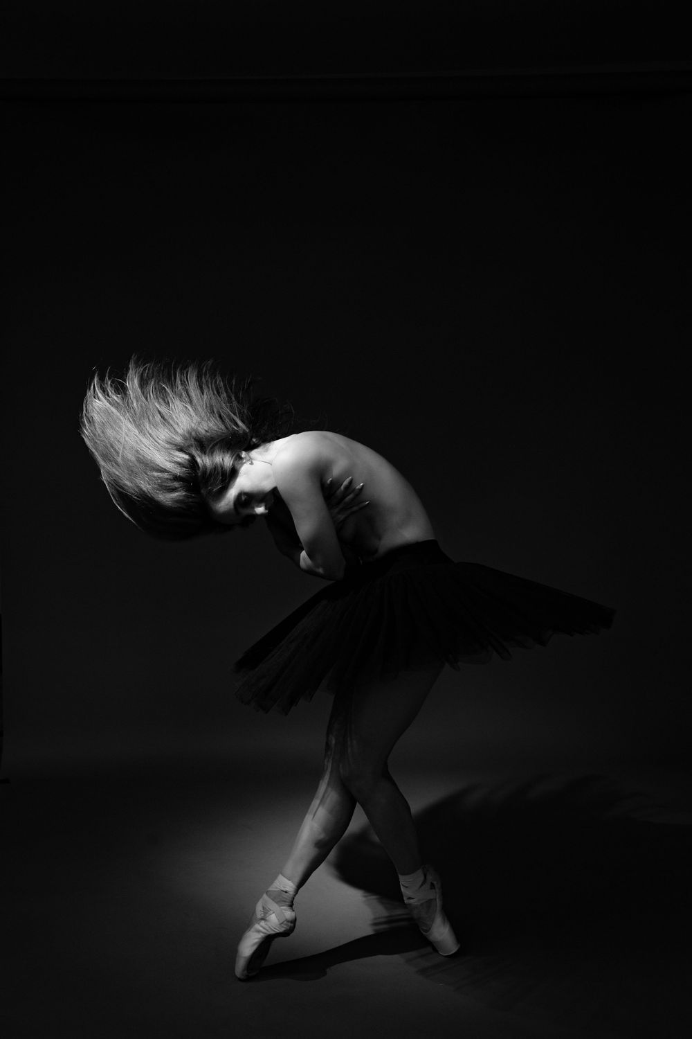 A dramatic black and white photo captures a ballet dancer in a tutu performing an elegant pose in the spotlight.