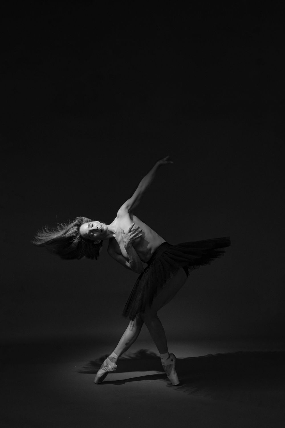 Dramatic black and white photos capturing expressive modern dance movements in a dark studio setting.