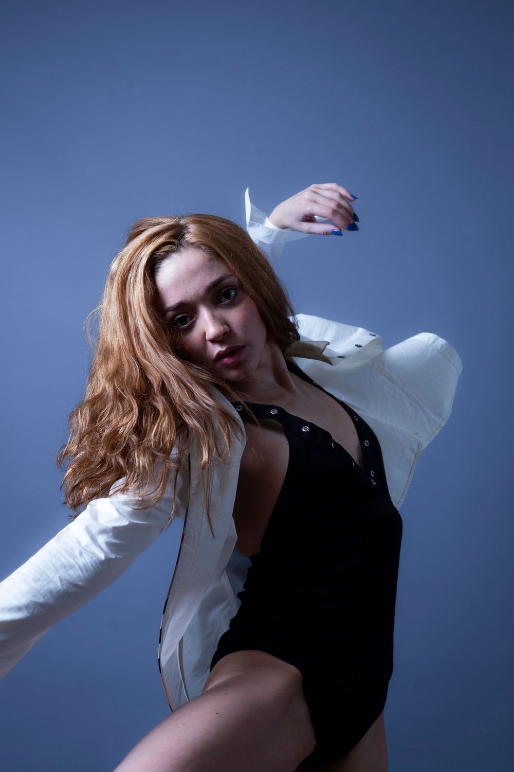 A dancer in a black leotard and white jacket strikes a dramatic pose against a blue background.