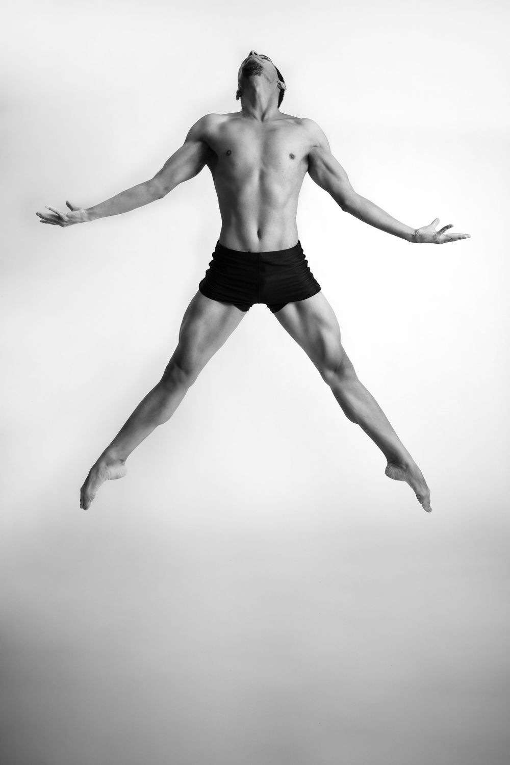 Black and white photo series showing a dancer leaping gracefully through the air in minimalist studio setting.