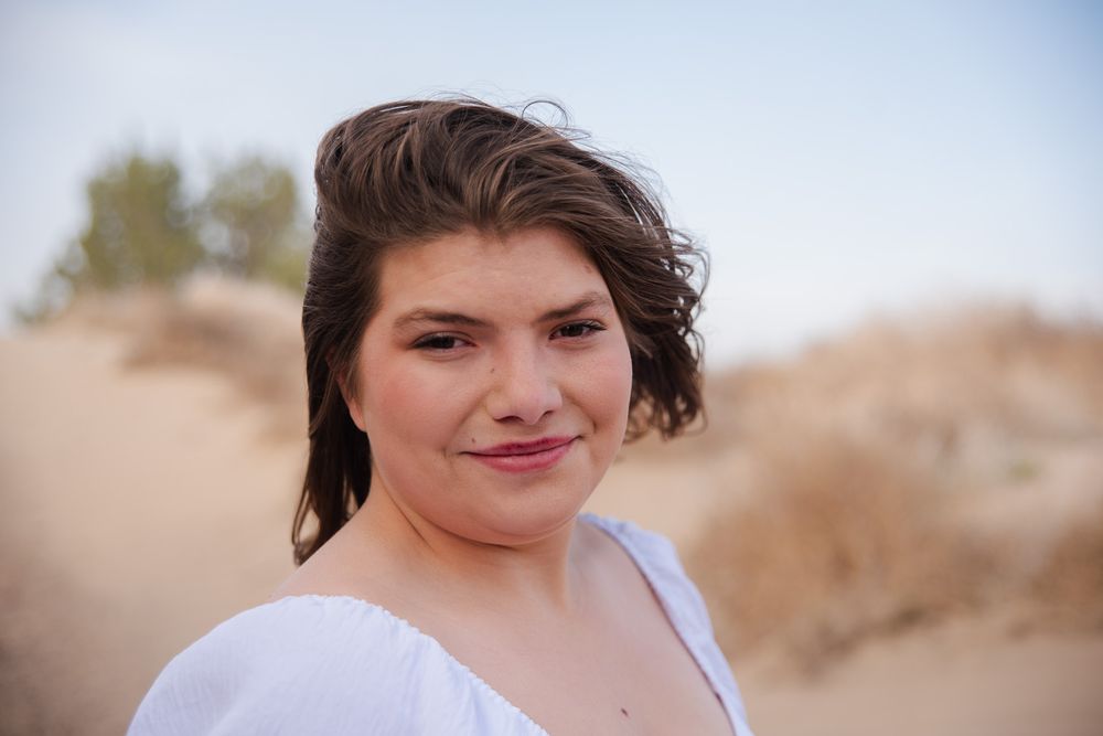 Close-up portrait of young woman with short brown hair smiling outdoors in desert.