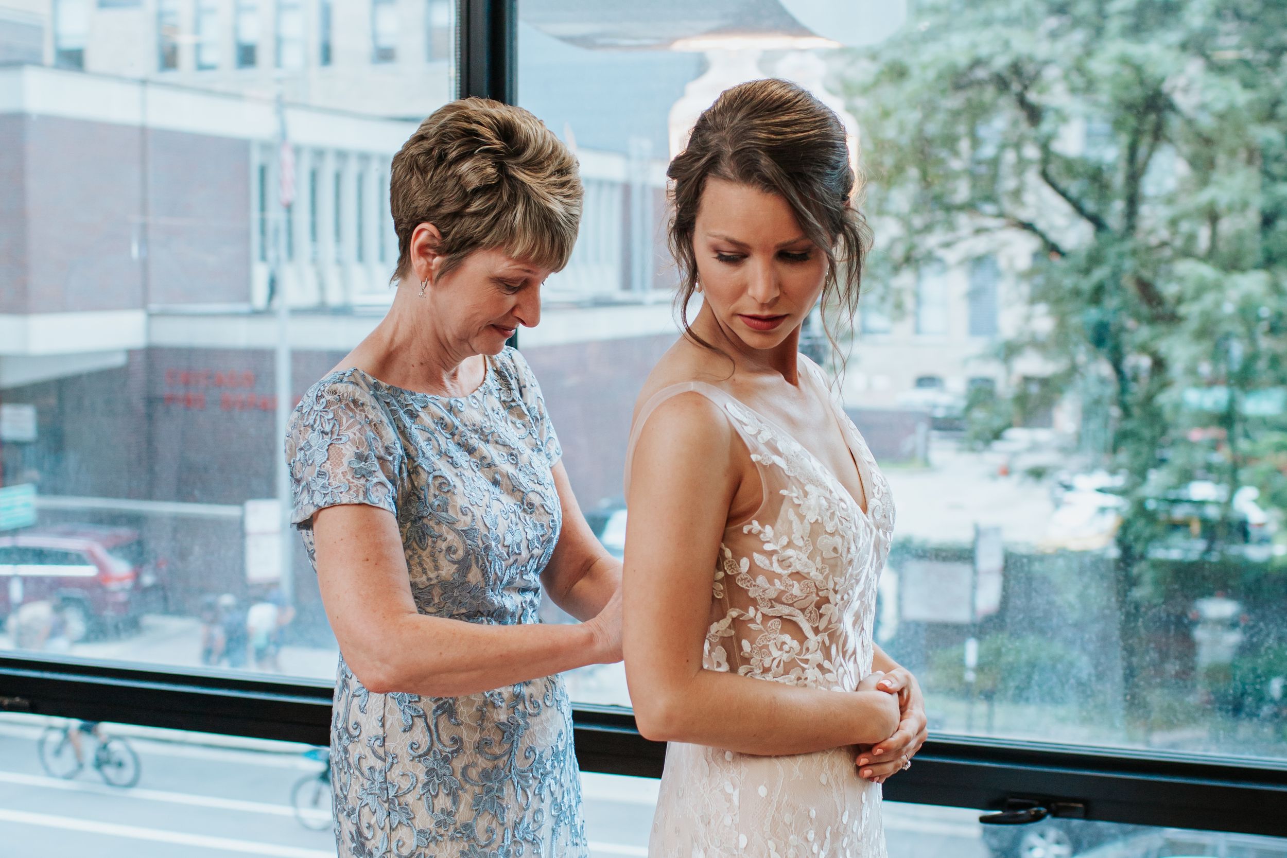 Two people in elegant formal attire share an intimate moment during a wedding celebration in a bright indoor space.