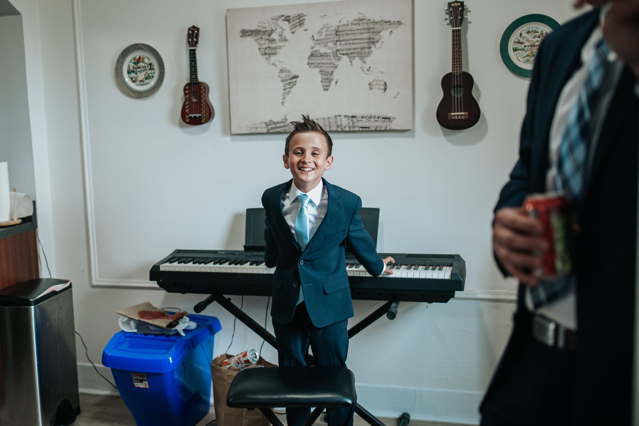 A room with musical instruments including guitars and a piano features world map artwork on white walls.