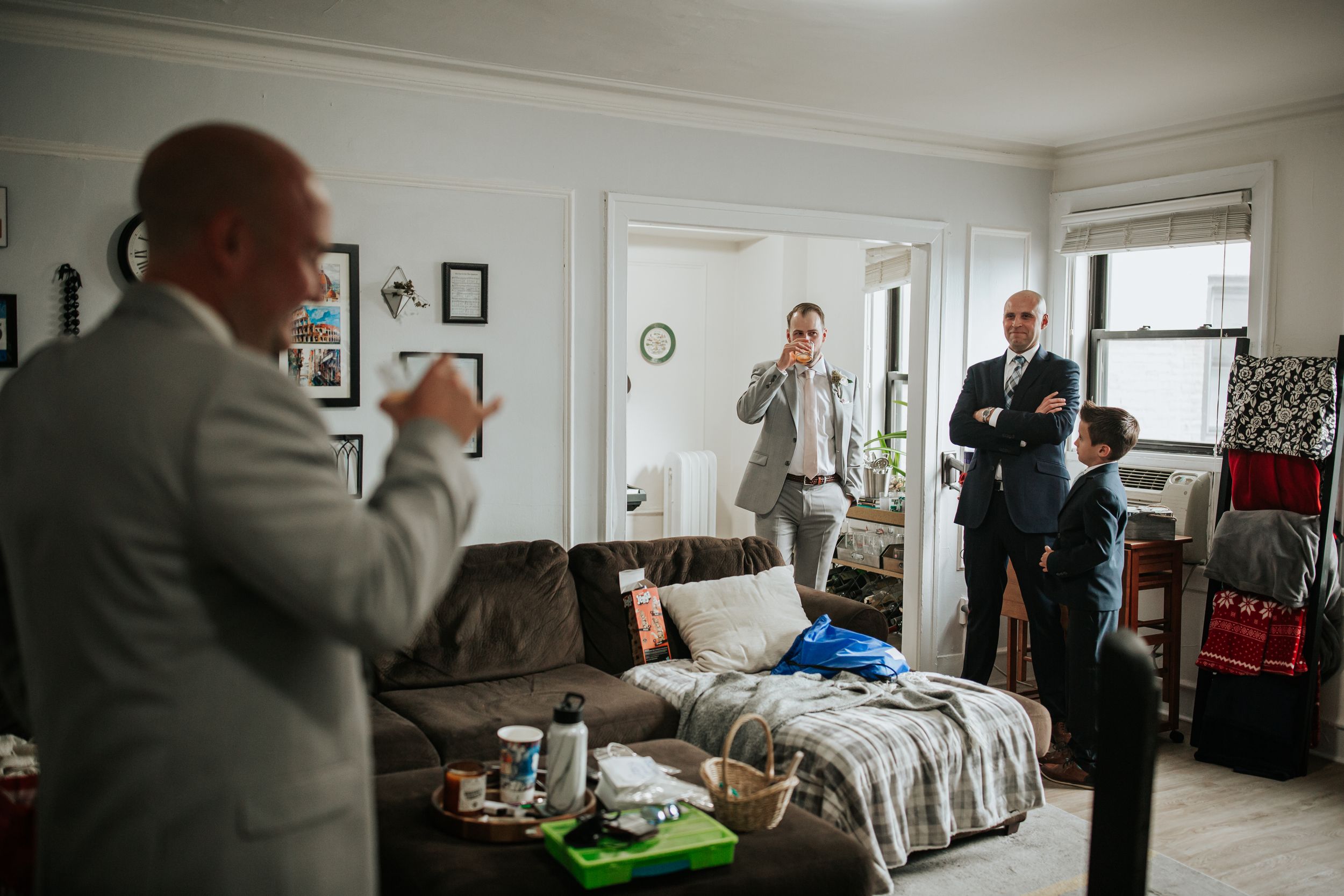 Three men in suits preparing in an apartment living room before an event.