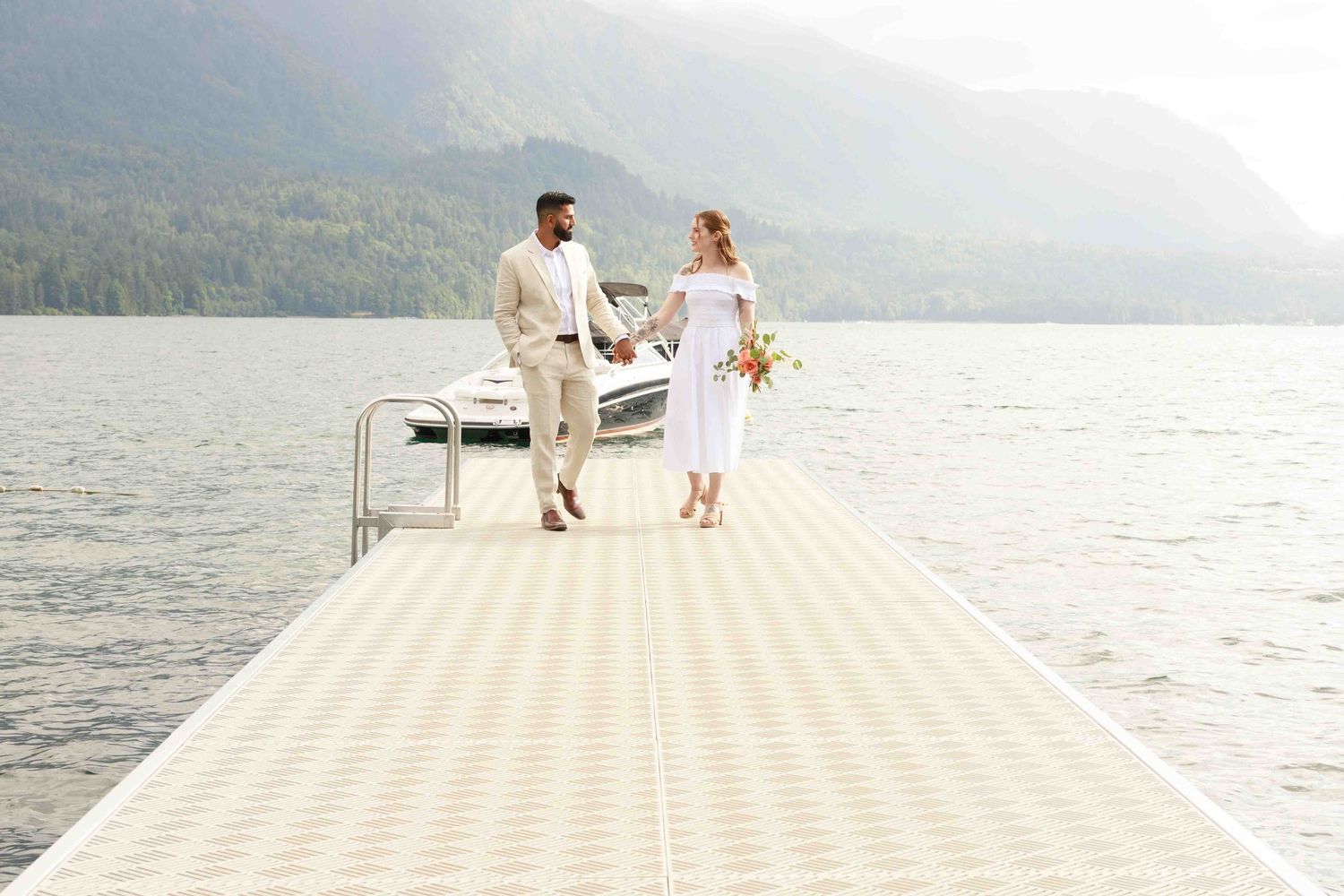 A couple stands together on a wooden dock overlooking a serene mountain lake.