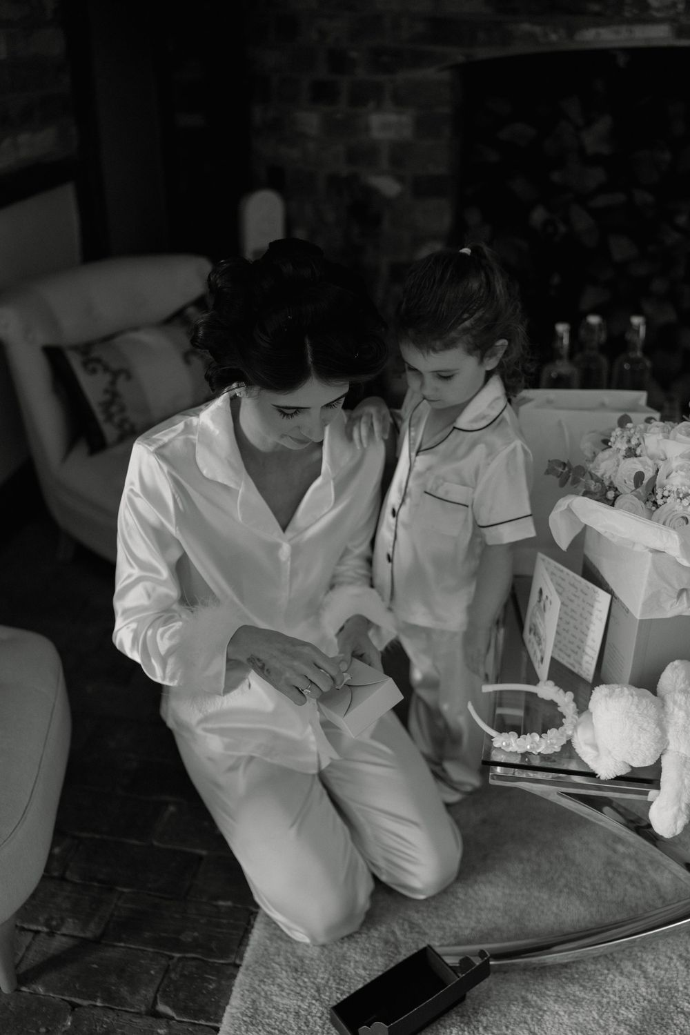 Black and white photo of a woman and young girl in matching white pajamas examining jewelry together indoors.