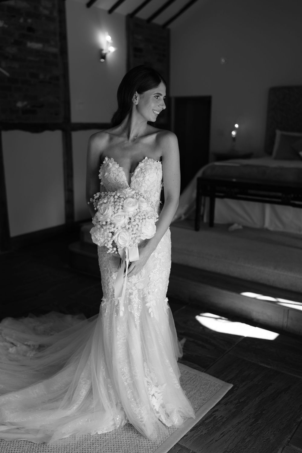 Bride in strapless lace mermaid wedding gown holding floral bouquet, elegant black and white bridal portrait.