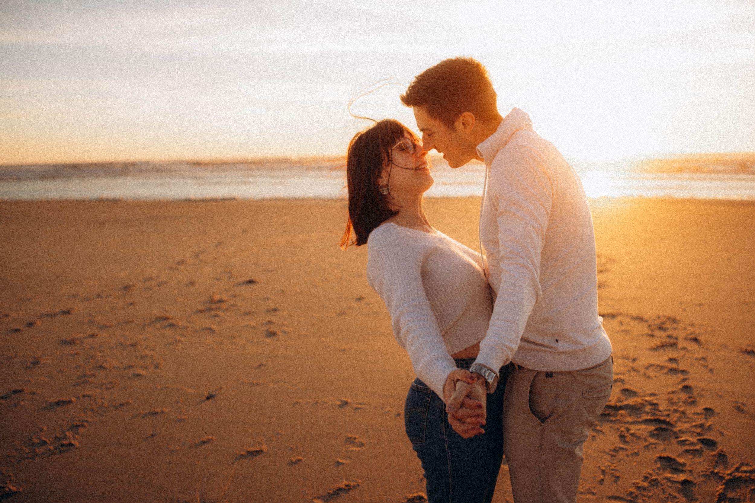 A couple shares a romantic moment at sunset on a beach with mountains in the background.
