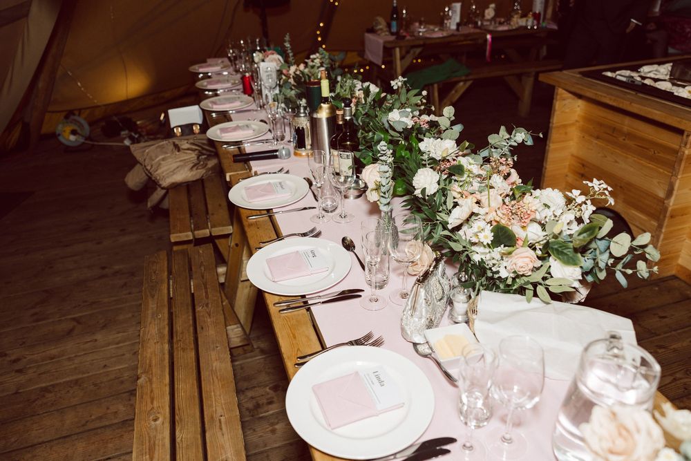 Elegant rustic wedding reception table settings with floral centerpieces and wine glasses in a warm wooden venue.