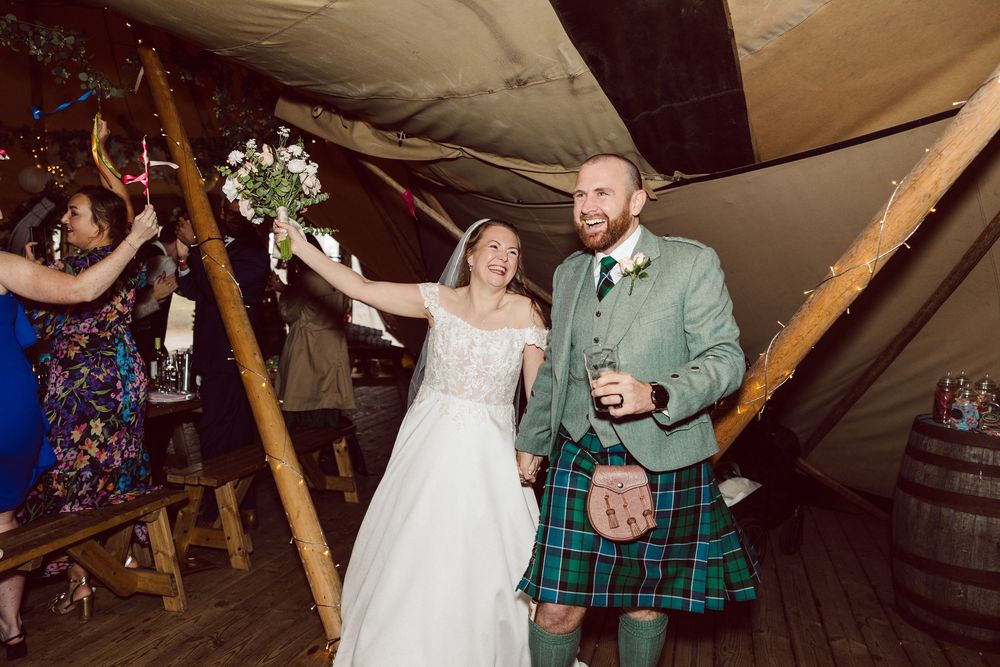 A couple dancing together at a rustic wedding reception venue with wooden beams and festive lighting.