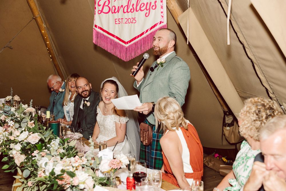 A wedding reception dinner inside a rustic tent with floral decorations and a pink neon sign on display.