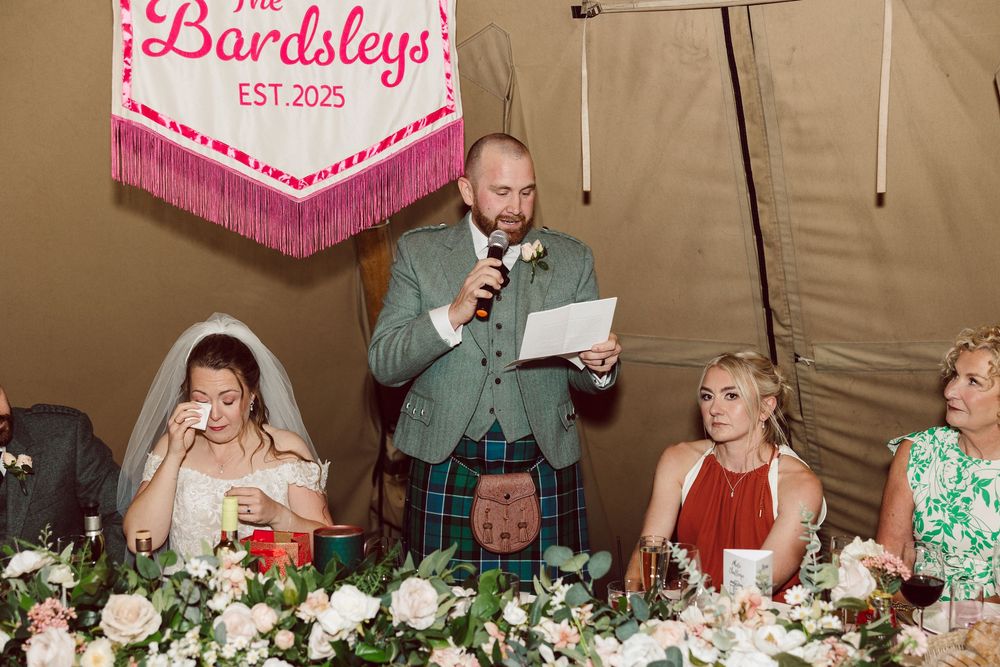 Wedding reception guests seated at long tables enjoying dinner and conversation in a decorated banquet tent.