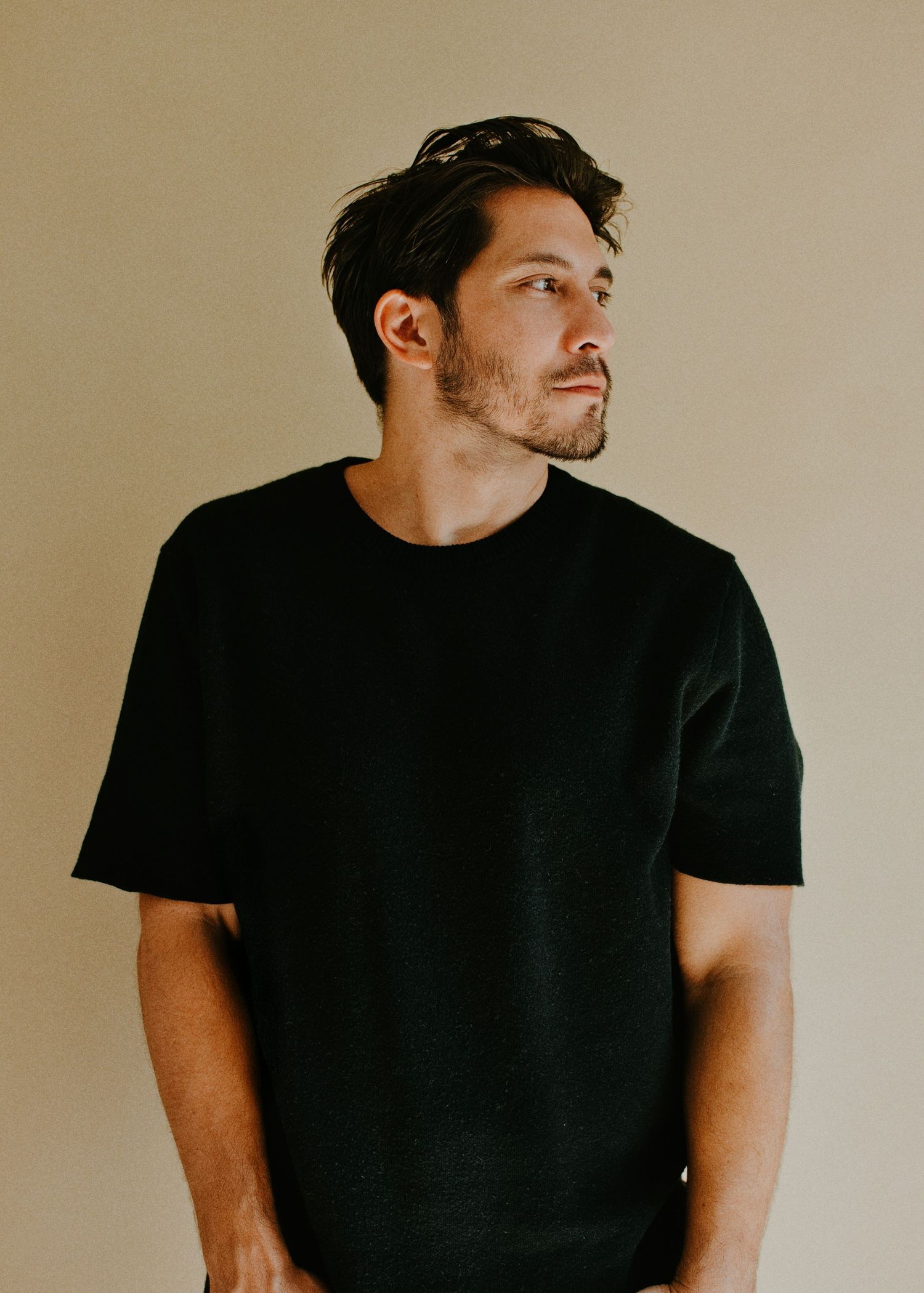 Portrait of someone in a black t-shirt looking to the side against a beige background.