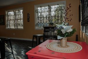 A red table with a potted plant sits near decorative iron windows in a dimly lit interior space.