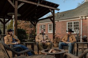 Guests gather around a rustic outdoor fire pit seating area with wooden benches at a brick building venue.