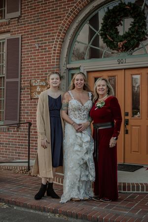 Three people stand together in front of a brick building with an arched doorway and holiday wreath.