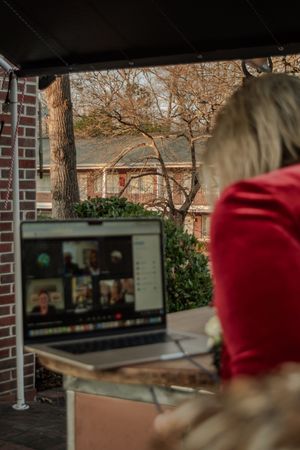 A laptop screen showing a video call is set up outdoors near a brick building.