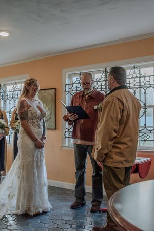 Wedding ceremony attendees gathered in an indoor space with decorative iron windows and peach walls.
