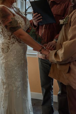 Close-up details of a wedding ceremony showing a white lace dress and tan jacket.