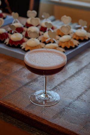 A pink cocktail served in a coupe glass on a rustic wooden surface.