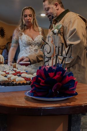 A wedding dessert table with red and blue decorative flowers and small cupcakes arranged on wooden surfaces.
