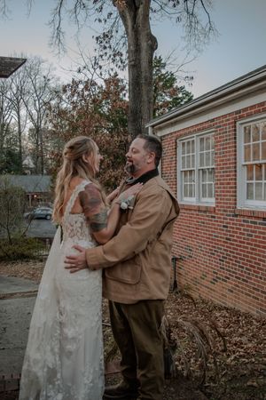 Couple shares intimate moment outside brick building during rustic outdoor wedding.