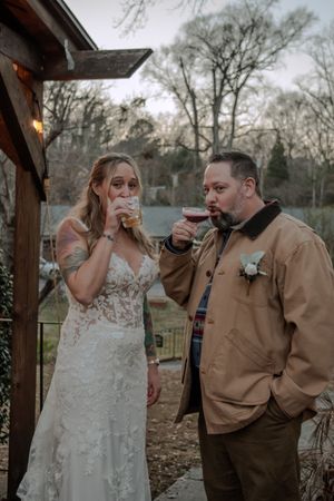 Wedding couple sharing drinks together under a rustic wooden pergola during their celebration.