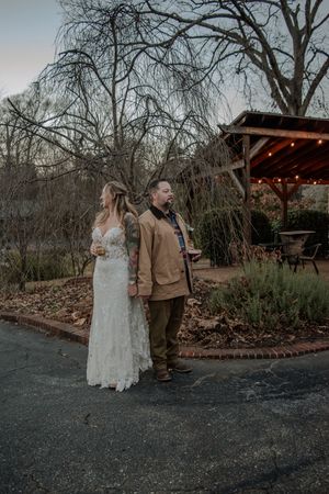 Wedding couple taking romantic photos in an outdoor garden setting with string lights and bare trees.