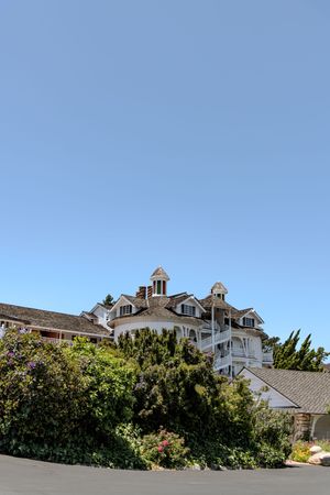 White mansion with dormers and cupolas sits against bright blue sky on sunny day.