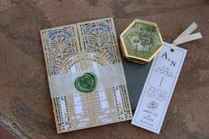 A collection of vintage-style wedding invitations and envelopes with ornate designs displayed on a textured surface.