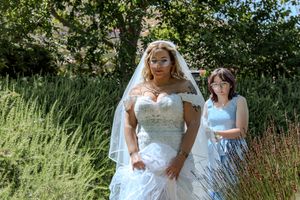 A bride in a white lace gown poses in a garden setting with tall grasses and greenery in the background.