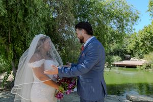 A wedding couple shares a romantic moment by a serene pond with willow trees in the background.