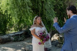 A joyful wedding moment captured under a weeping willow tree with a beautiful purple bouquet.