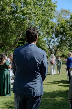 Wedding guests gather on sunny lawn during outdoor ceremony.