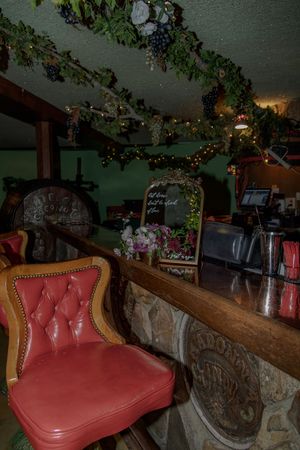 Cozy restaurant interior with red leather booth seating and rustic wooden beams decorated with twinkling lights and greenery.