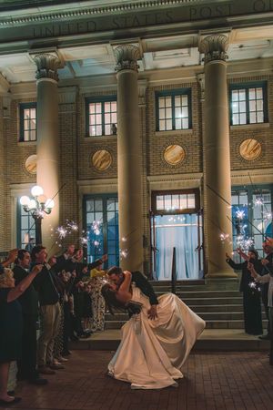 A couple shares their first dance at a grand venue with classical columns and ornate architecture illuminated at night.