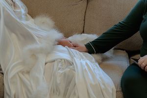 A person in a dark jacket demonstrates folding a white sheet or blanket in a step-by-step sequence.