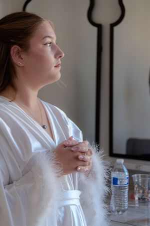 Person in white robe sitting at table with feather and glass jar in contemplative side profile pose.