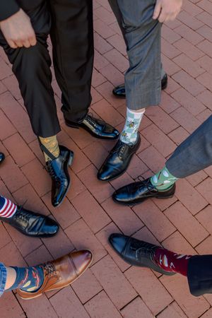 A line of people's feet showing various dress shoes and sneakers on a brick walkway with a small American flag visible.