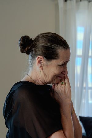 A person in dark clothing covers their face with their hands in an emotional moment.
