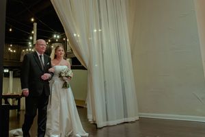 Wedding party gathers in an elegant indoor venue with white curtains and formal attire for a special celebration.