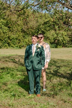 Wedding couple shares a playful first look moment in a sunny outdoor garden setting with green trees.