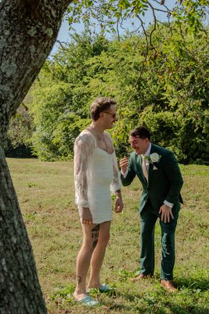 A couple shares a playful moment dancing together on a sunny day in a grassy field with trees in the background.
