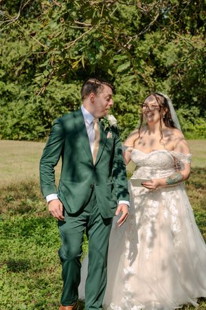 Newlywed couple shares intimate moments in a lush garden setting wearing emerald green suit and white lace gown.