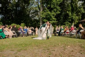 Outdoor wedding ceremony setup with rows of chairs on a grassy hillside under trees.