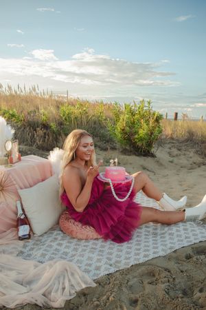 Person in a pink tulle dress lying on a blanket at the beach during golden hour.