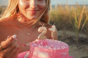A pink birthday cake with sparkler candles glows warmly at sunset on the beach.
