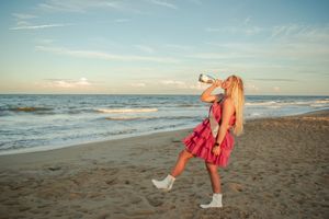 Athletic figure in red activewear performs dynamic stretches on a sandy beach at sunset.