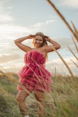 A figure in a flowing pink dress dances through tall grass at sunset in a dreamy outdoor photoshoot.