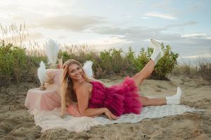 A person in a flowing gown poses gracefully on a sandy beach at sunset.